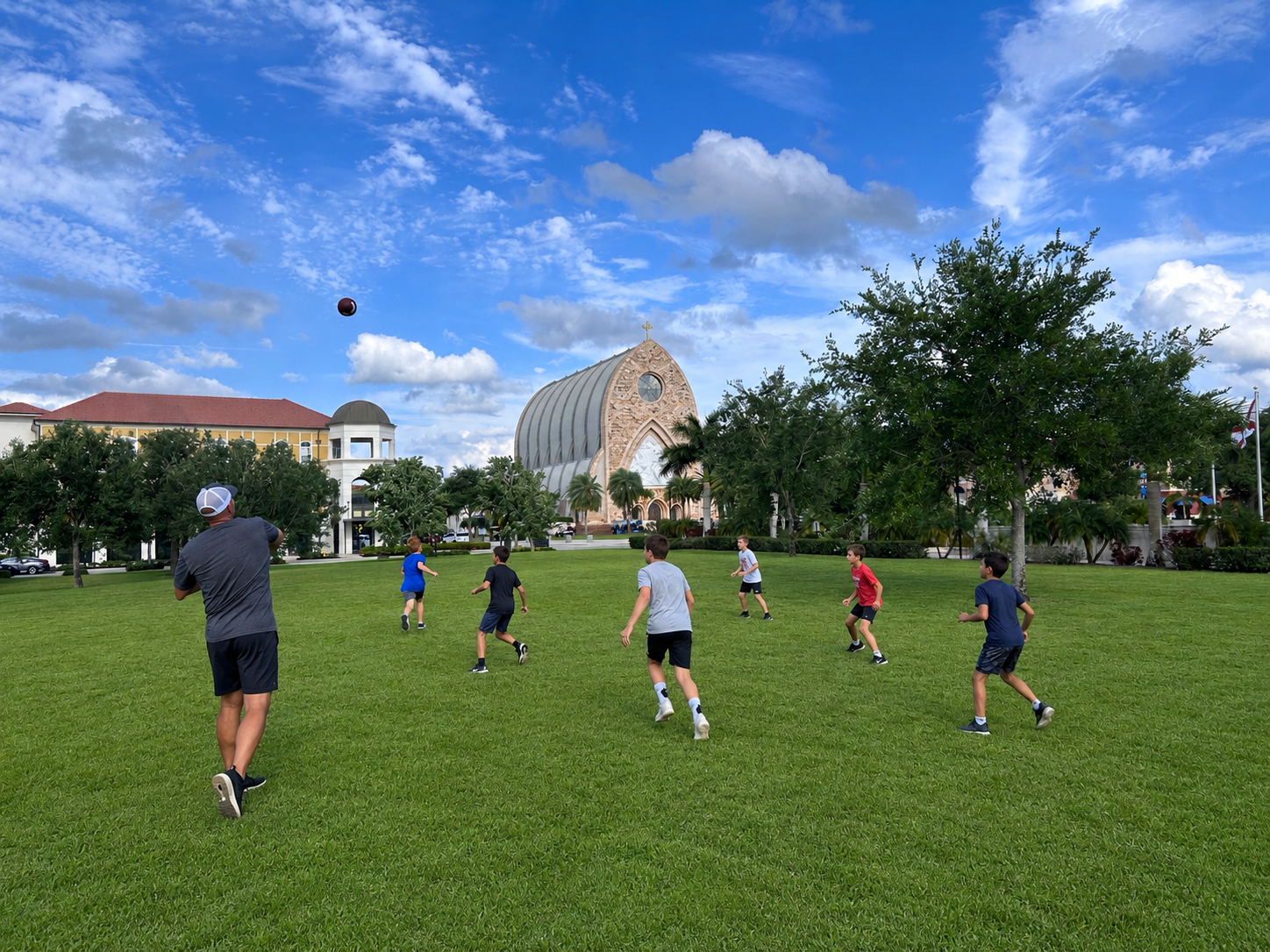 Coach Andrew throwing a football to youth athletes with the Ave Maria church in the background